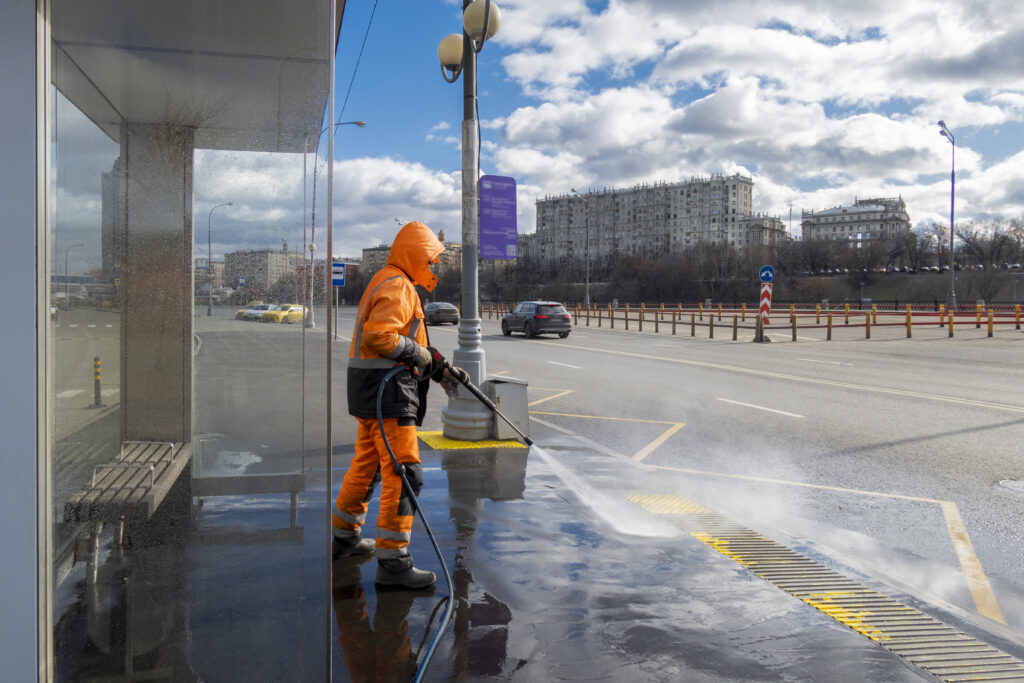 Road worker cleaning city street with high pressure power washer, cleaning dirty public transport stops, Moscow, Russia