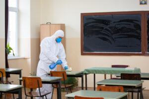 Worker sprays disinfectant as part of preventive measures against the spread of the COVID-19, coronavirus in schools. Preparing for the new school season.